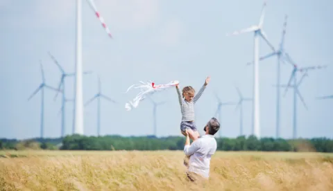 People on a field with wind turbines in the background
